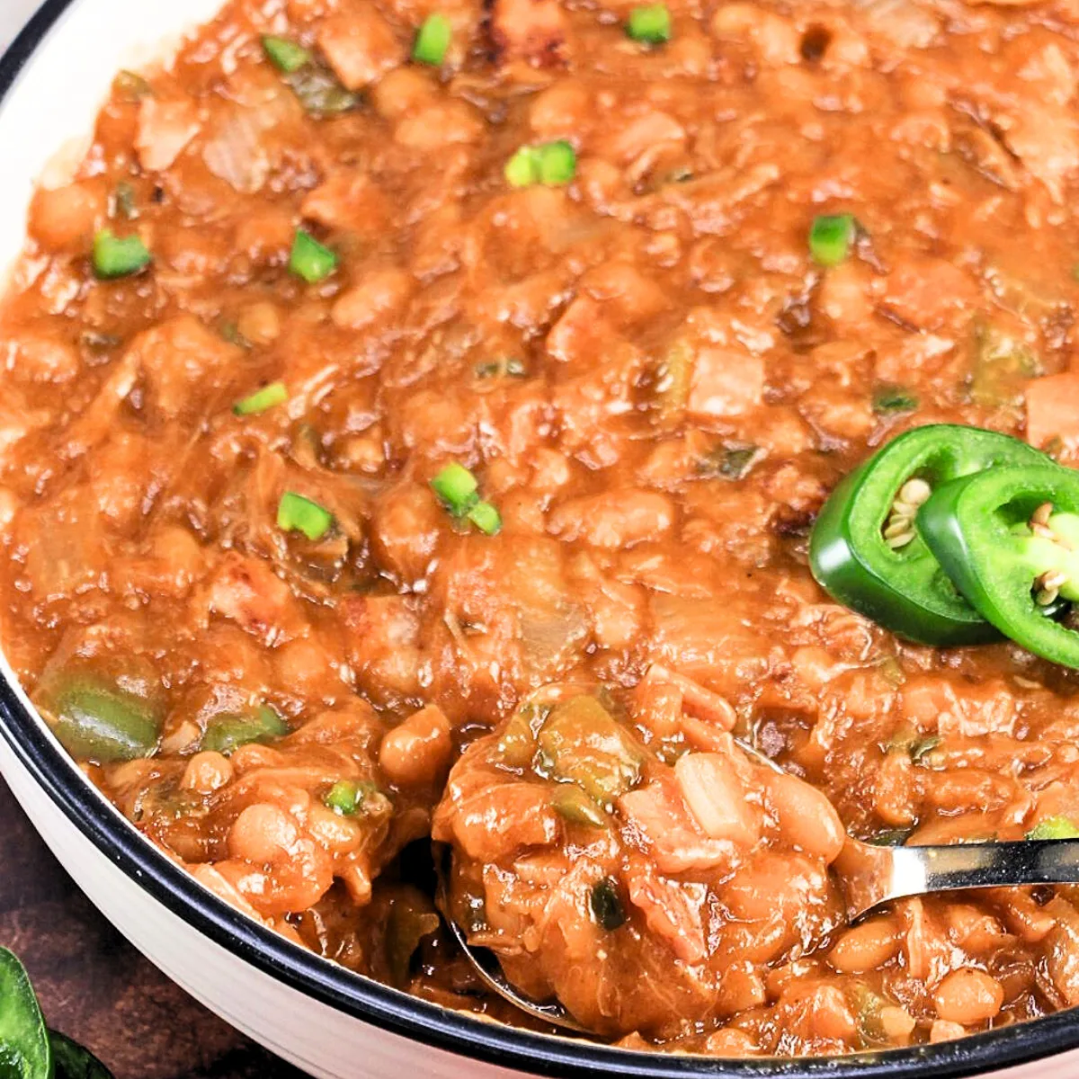 Angled view of a white bowl filled with baked beans garnished with diced jalapeno peppers - Hostess At Heart