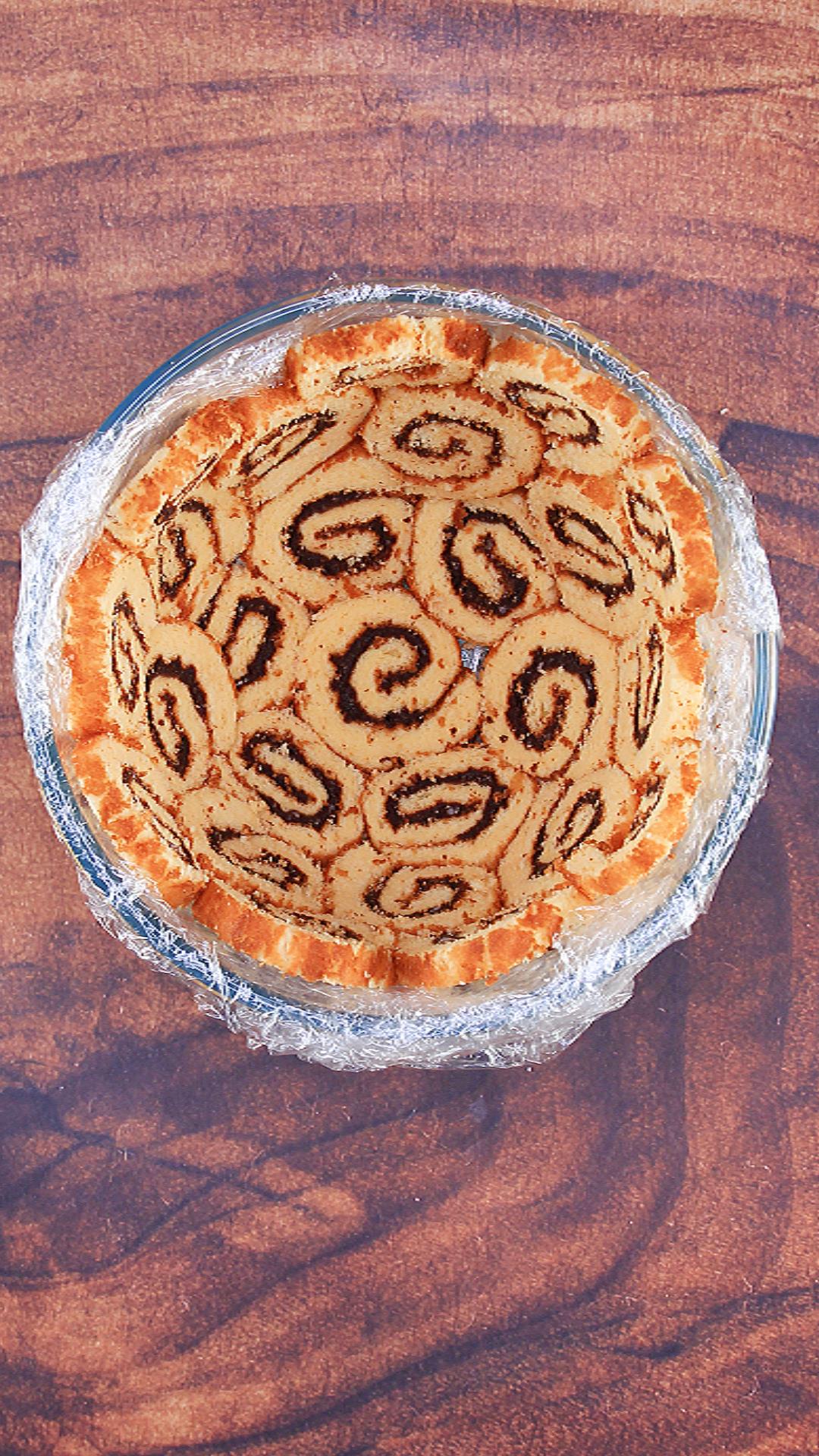 A bowl lined with plastic wrap and filled with slices of cake swirrled with buttercream.