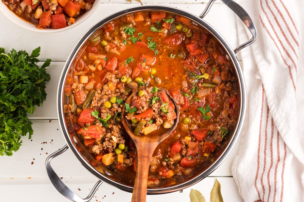 Hamburger Vegetable Soup Recipe in a large stock pot with a wooden spoon inside. Top down view. Hostess At Heart