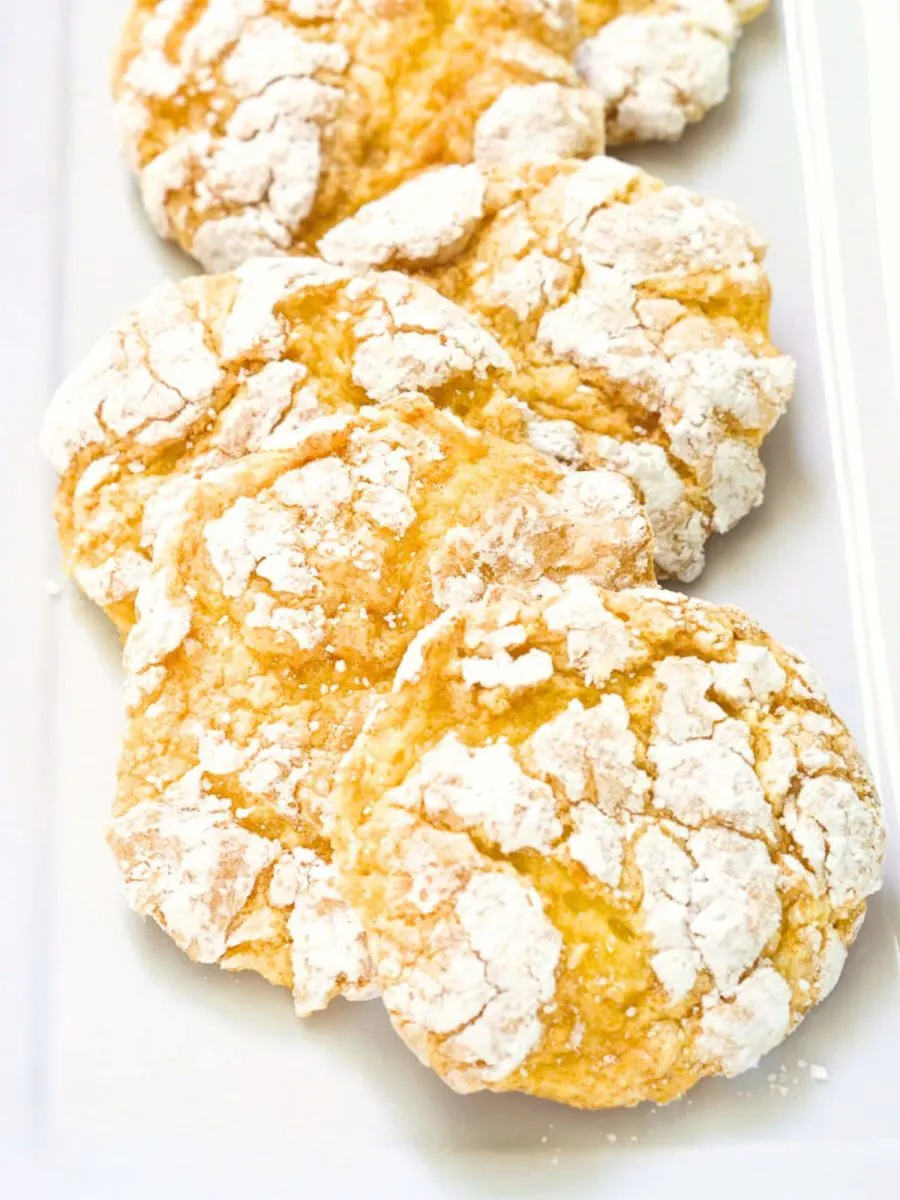 Front table view of yellow Lemon Cake Mix Cookies layered in a row on a white plate. Hostess At Heart