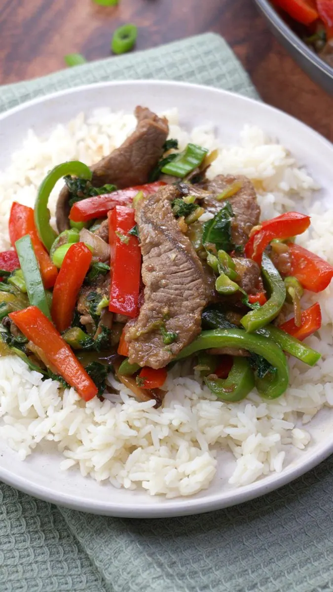 Mongolian beef stir fry over rice on a white plate, close up of finished dish.