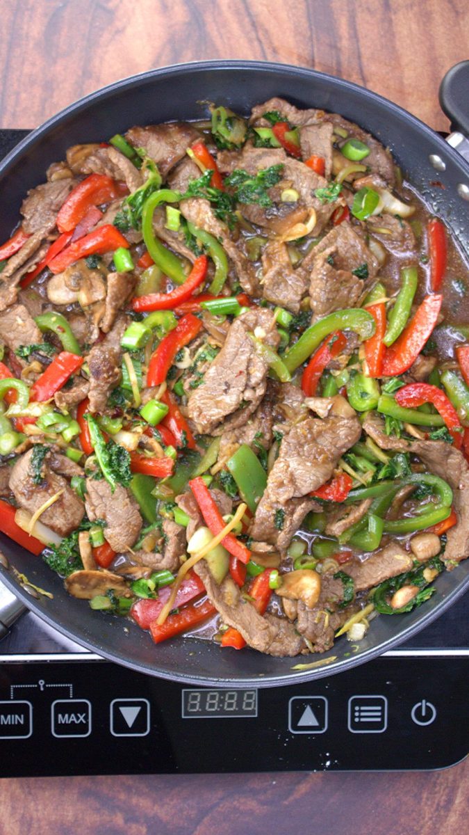 A skillet filled with mongolian beef stirfry with veggies and garnished with green onions Hostess At Heart