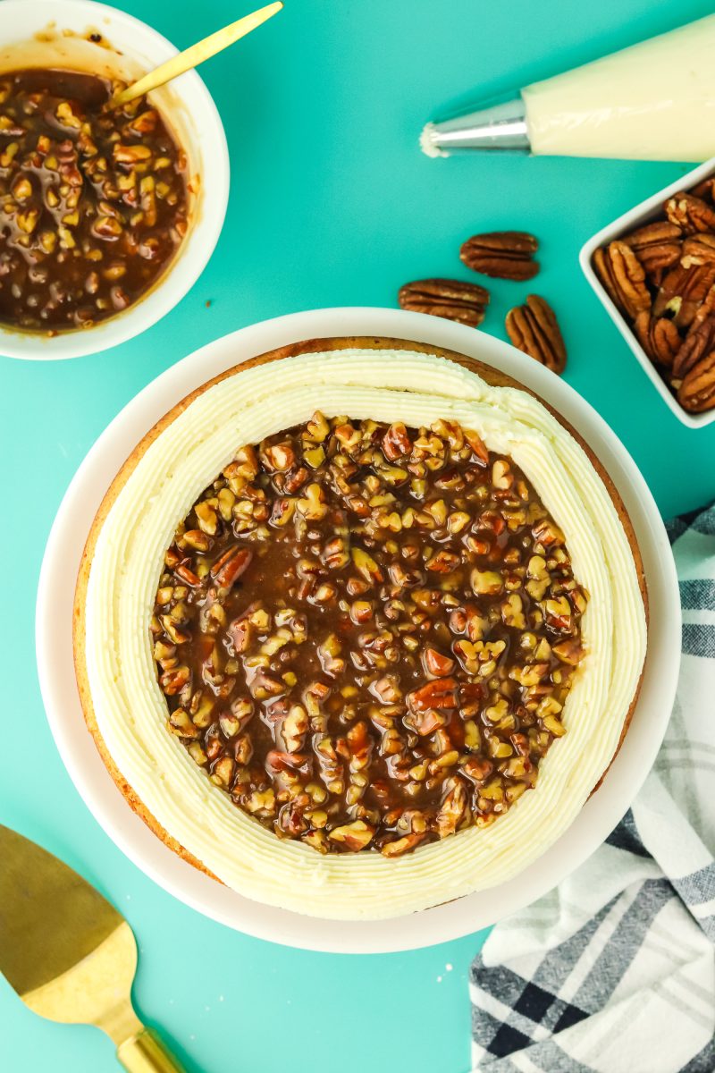 Homemade pecan pie filling topping a cake between a frosted piped border - Hostess At Heart