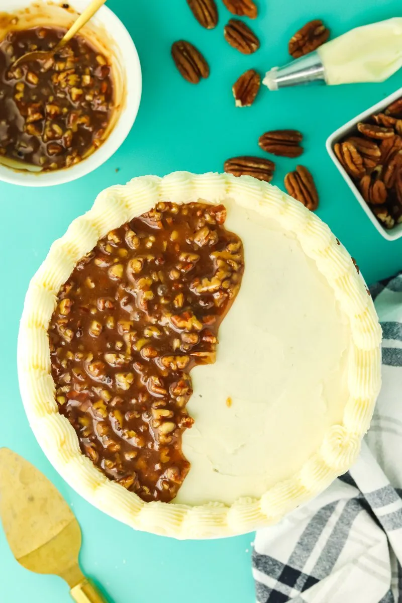 Top down view of a buttercream frosted and edged round cake. Pecan pie filling is being applied over the top. Hostess At Heart