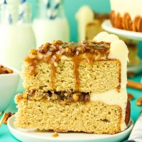 Tableview image of a slice of pecan pie layer cake filled with praline and frosted over the sides. The top has a layer of pecan filling that's dripping down the uncut cake. Hostess At Heart