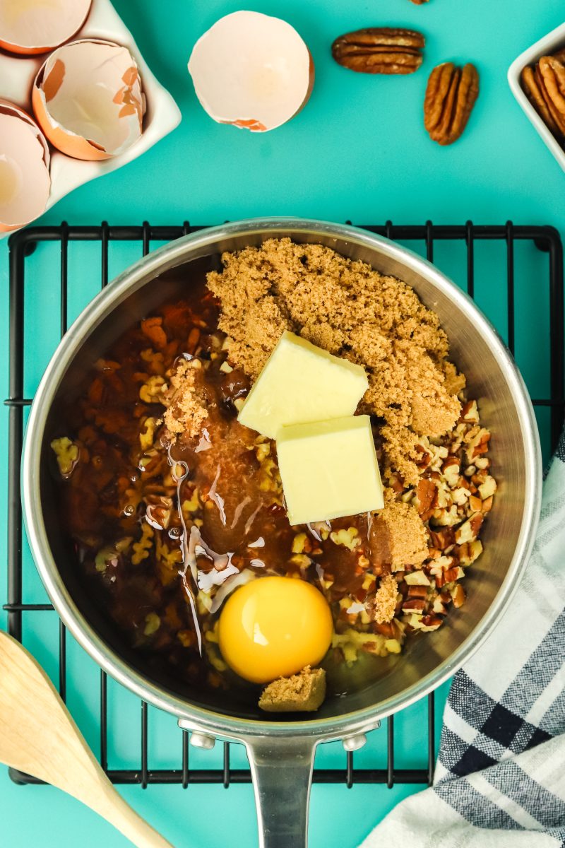 Pecan filling ingredients added to a saucepan including pecans, brown sugar, eggs, corn syrup, and butter.