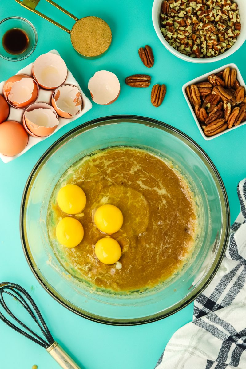 3 eggs added to a mixing bowl filled with a mix of sugar and melted butter - Hostess At Heart