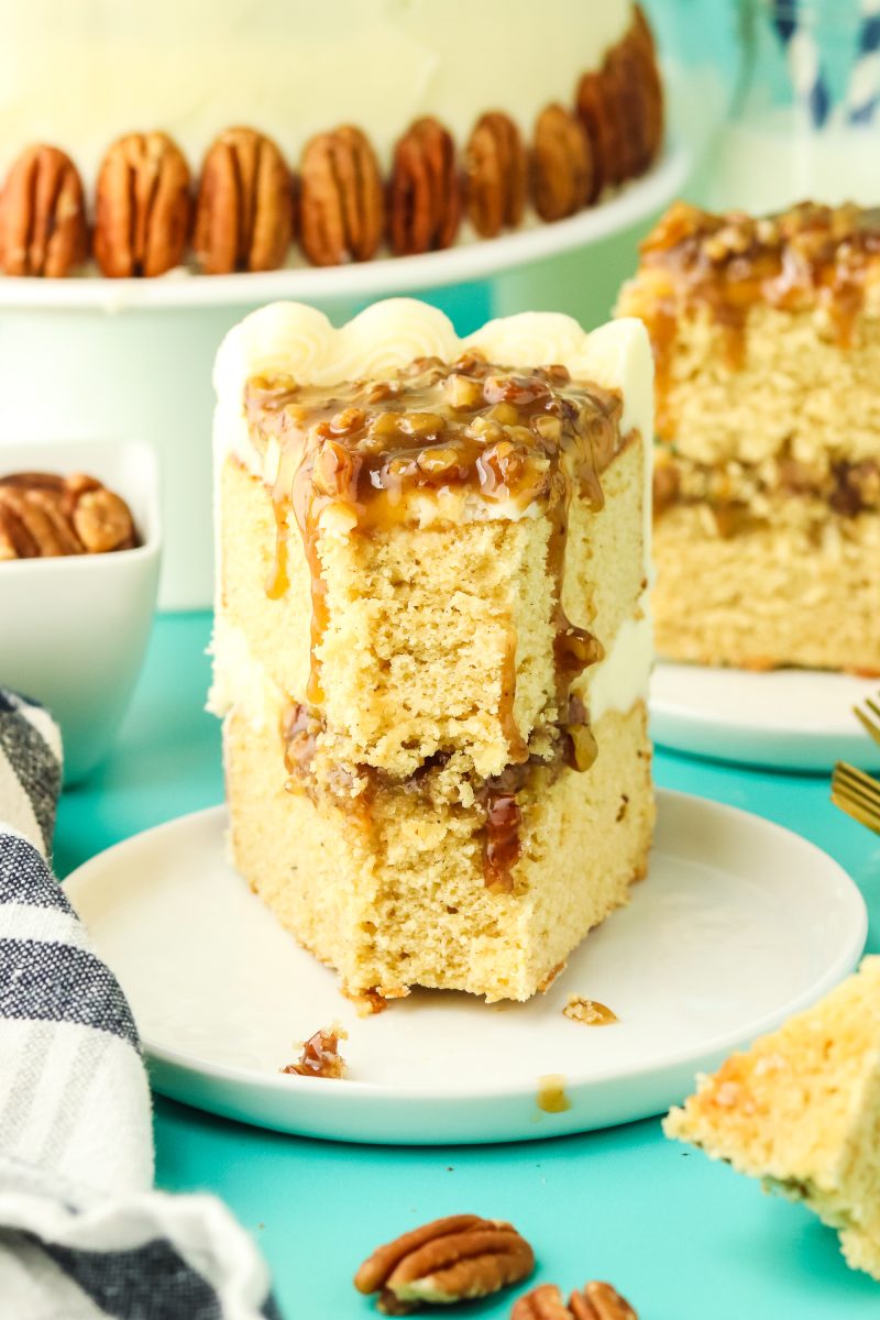 A slice of two layer cake with the front forkful missing showing a layer of pecan filling between the cake layers and buttercream frosting spread over the sides - Hostess At Heart