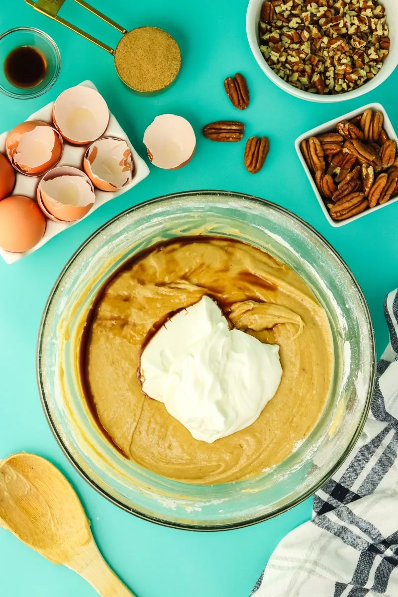 Top down view of sour cream and vanilla extract added to cake batter in a mixing bowl. Hostess At Heart