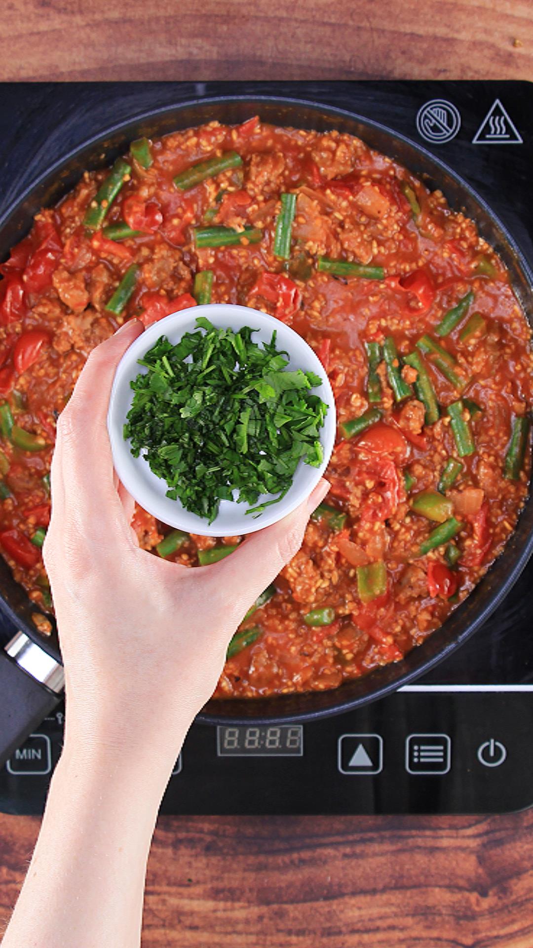 Adding cilantro to the bulgur wheat sausage dish.