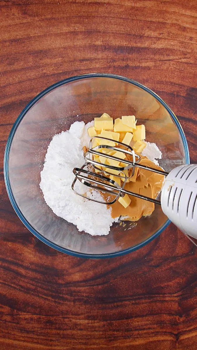 A mixing bowl filled with sugar, peanut butter, and butter.