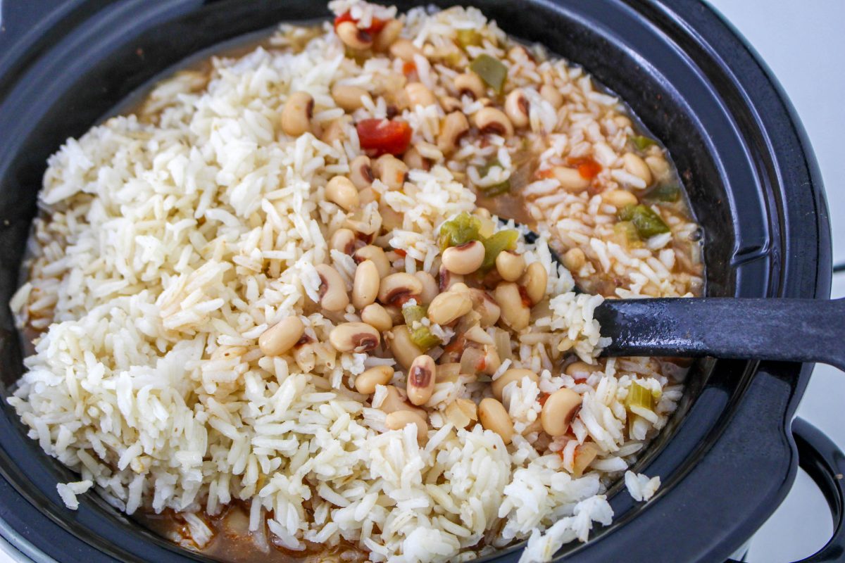 The bowl of a crock pot with rice being added to cooked black eyed peas - Hostess At Heart