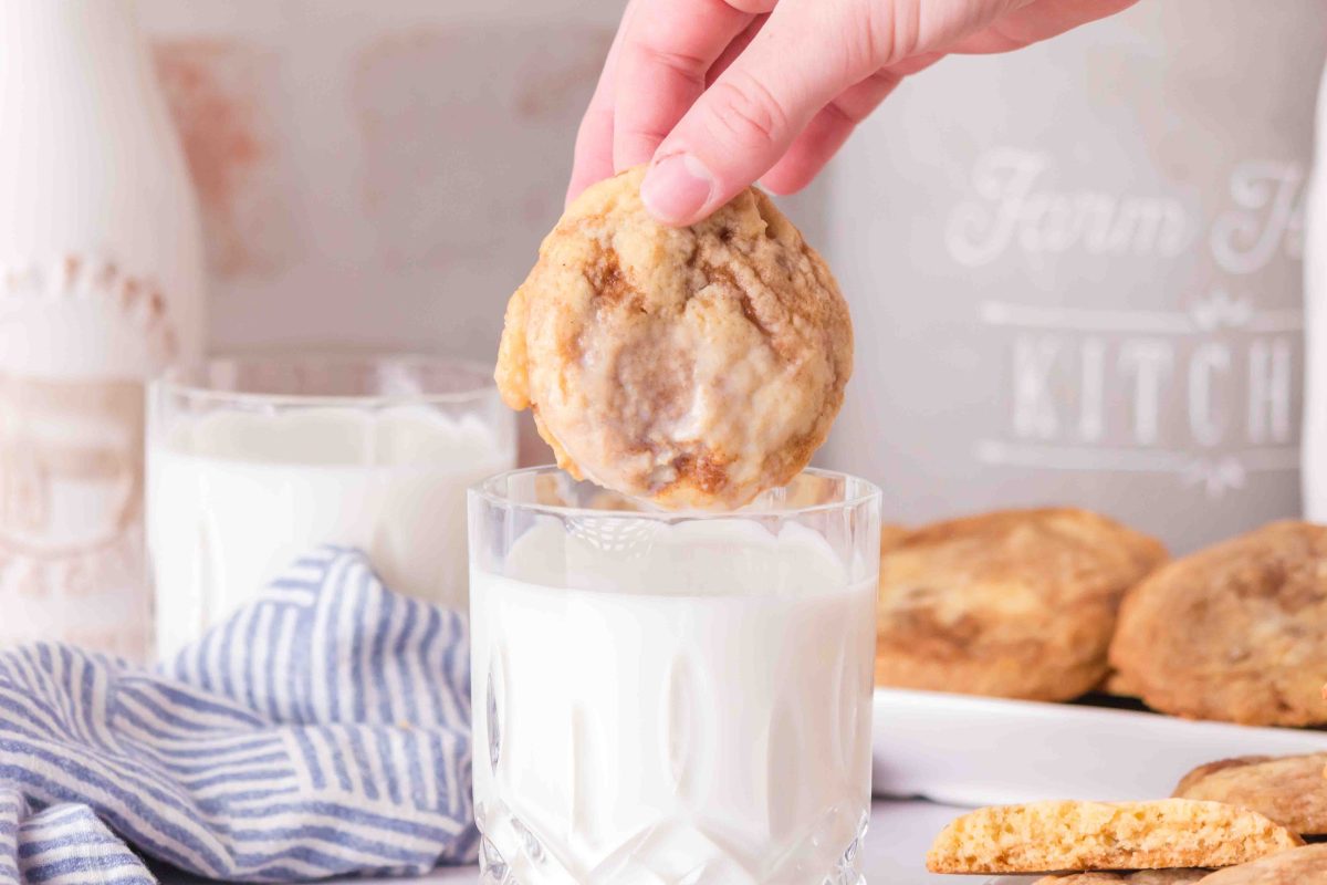 A warm cinnamon cookie is dipped in a glass of milk, and a plate of cookes is sitting in the background.