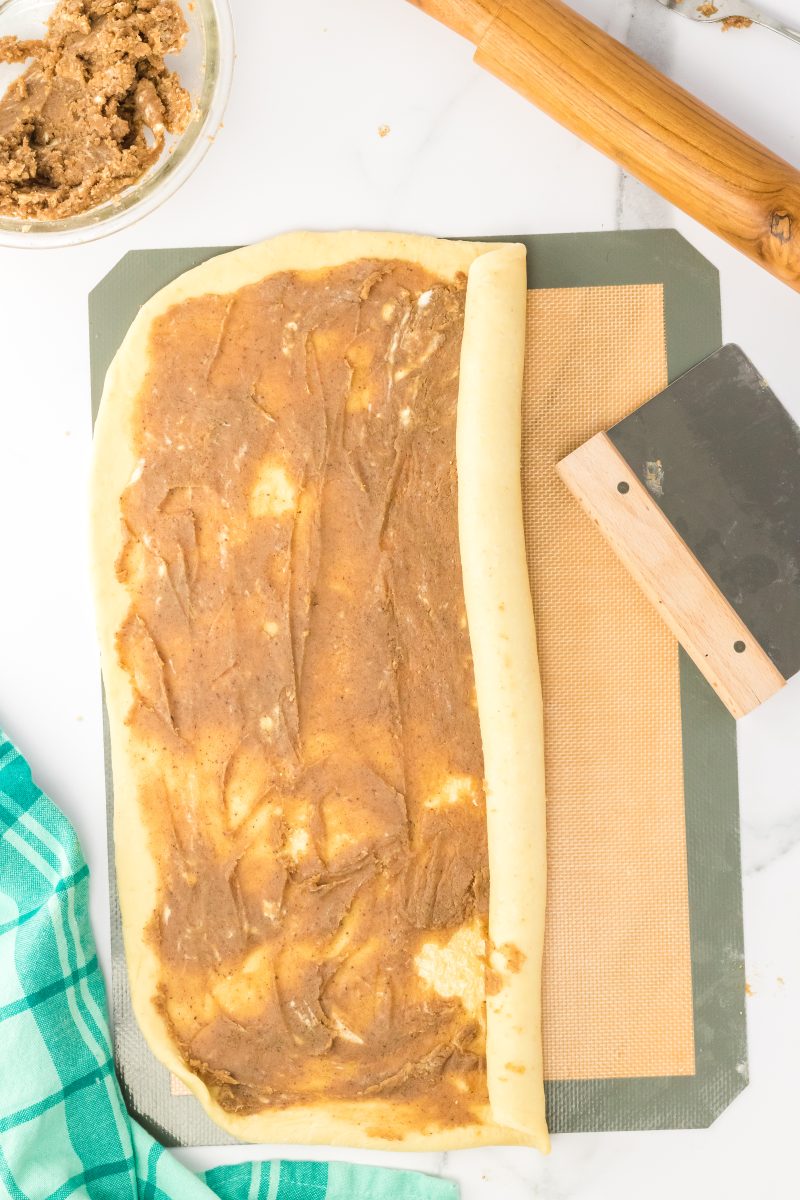 A long edge of rolled bread dough being rolled into a tube shape over filling