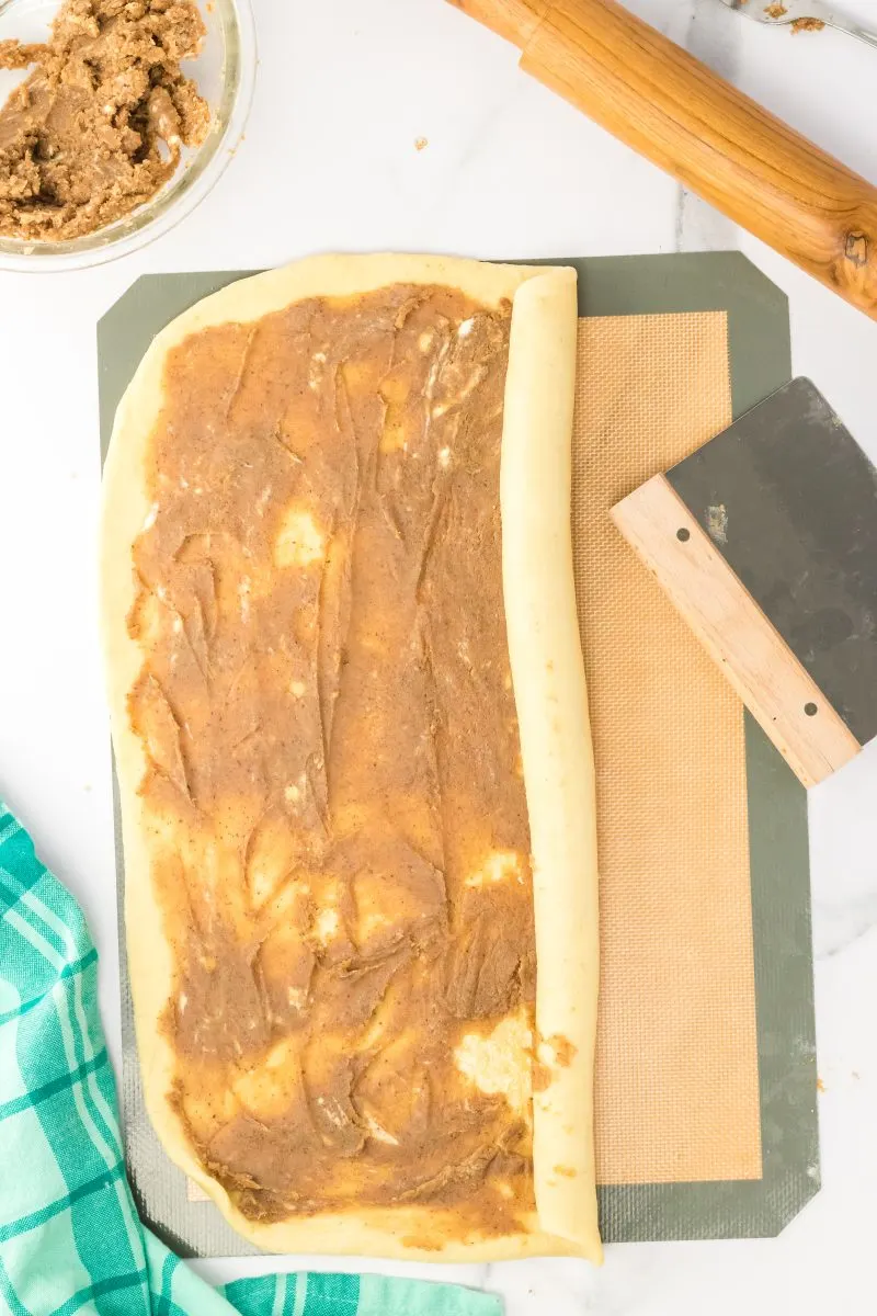 A long edge of rolled bread dough being rolled into a tube shape over filling