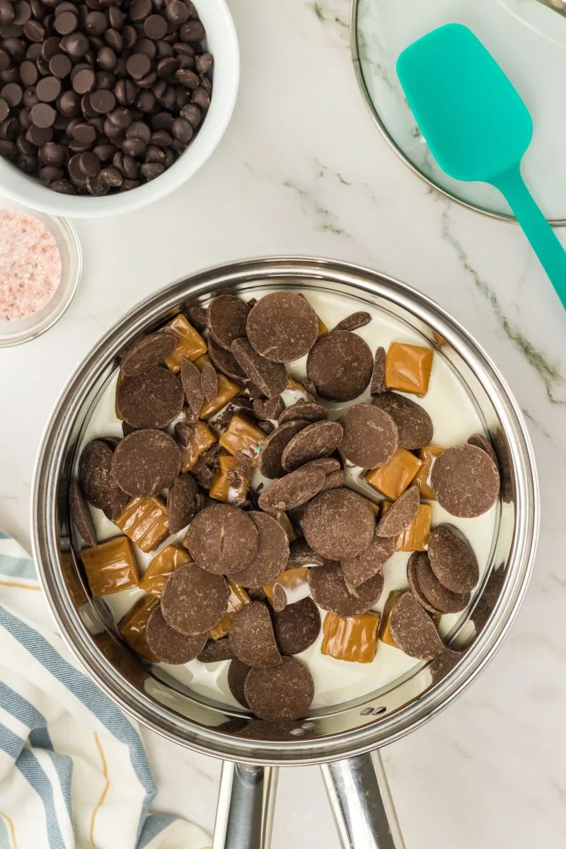 A saucepan with cream, chocolate melting wafers, and caramels.