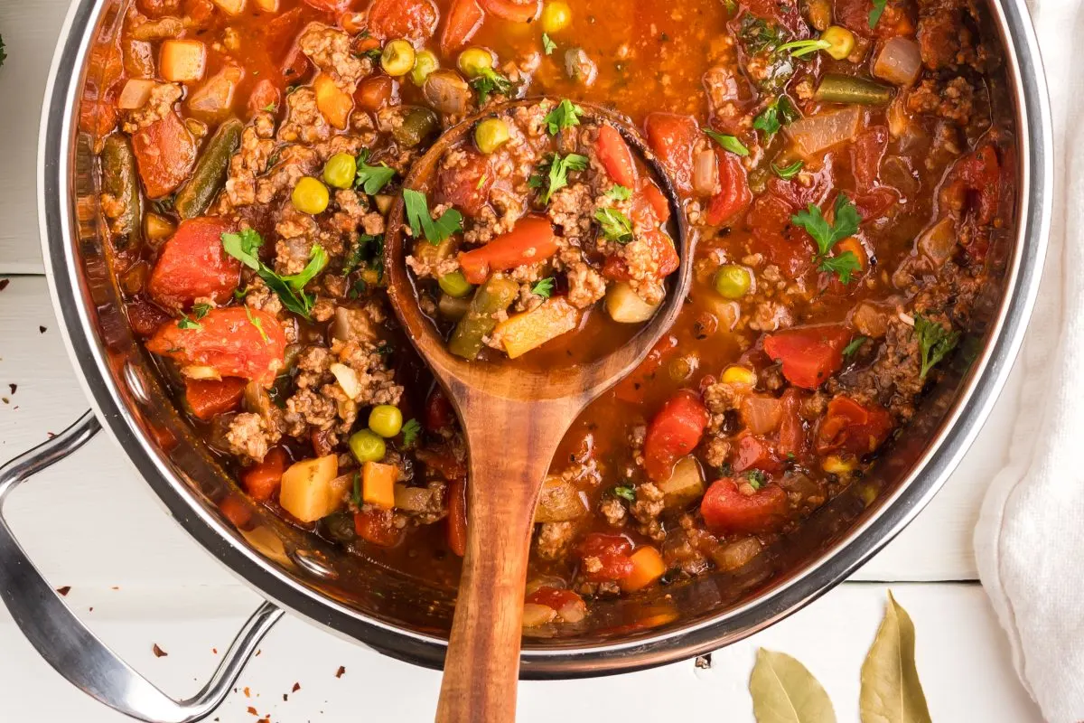 Very close up picture of Hamburger Vegetable Soup in a large stock pot with a wooden spoon inside. Top down view. Hostess At Heart