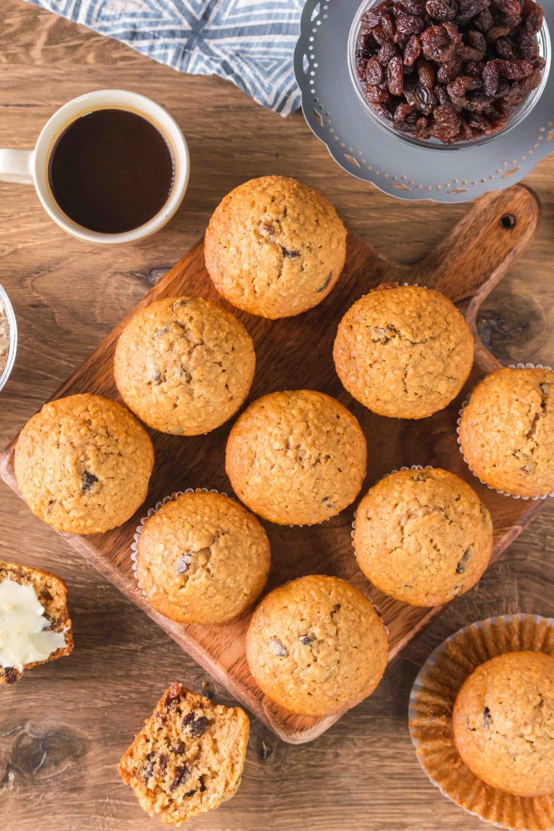 Top down image with oatmeal raisin muffins, a cup of coffee, and a bowl of raisins on a table.  Hostess At Heart