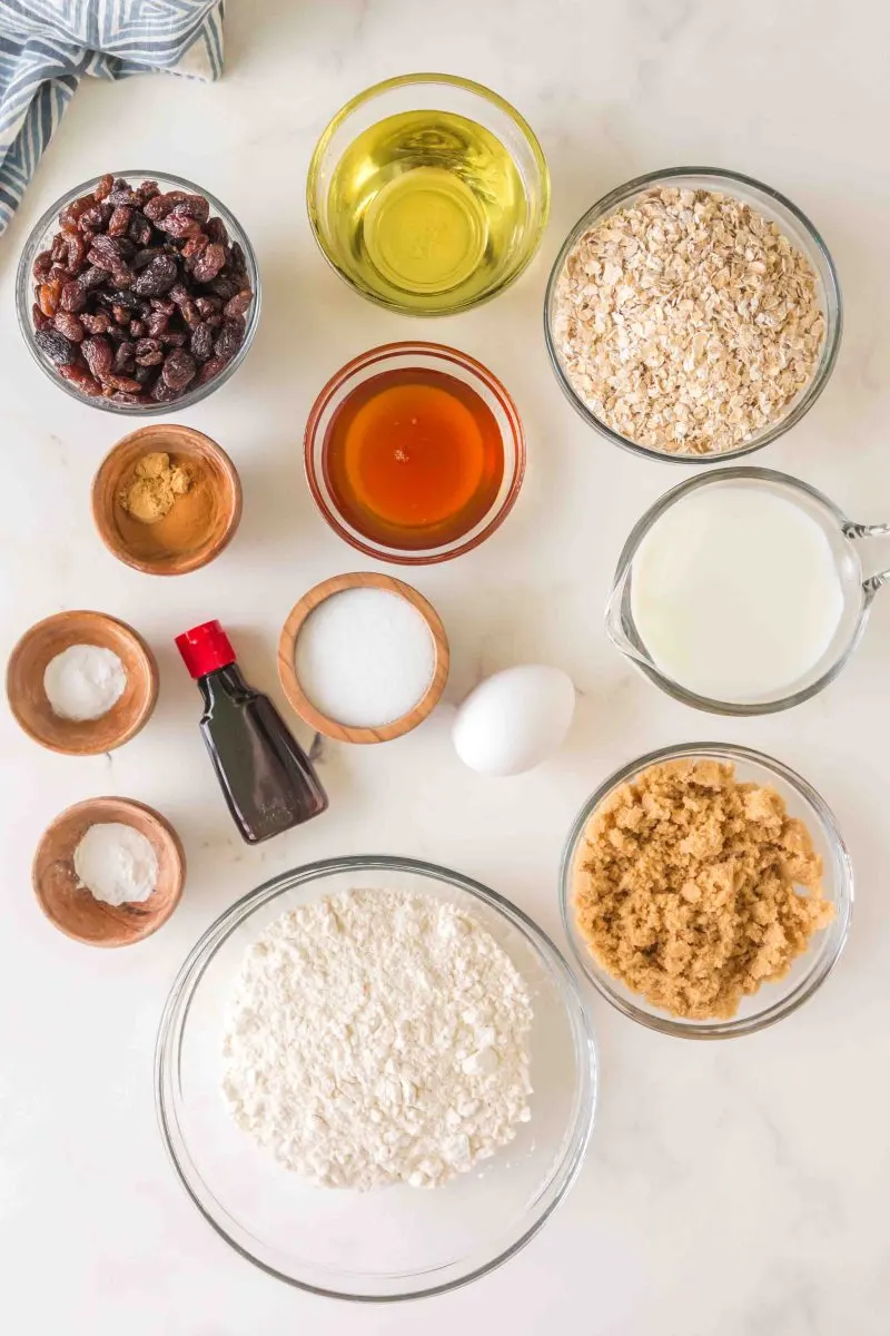 All of the ingredients for the recipe are pictured: Raisins, oil, oatmeal, cinnamon, honey, salt, baking soda, vanilla, milk, eggs, baking powder, flour, and brown sugar.