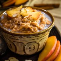 Angled view of a bowl of cooked steel cut oats topped with sliced peaches and almond slivers.