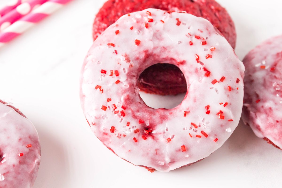 Close up of red velvet donut with cream cheese glaze and red sprinkles.