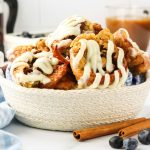 Sideview of a basket filled with beautifully baked cinnamon roll popovers topped with a cream cheese glaze - Hostess At Heart