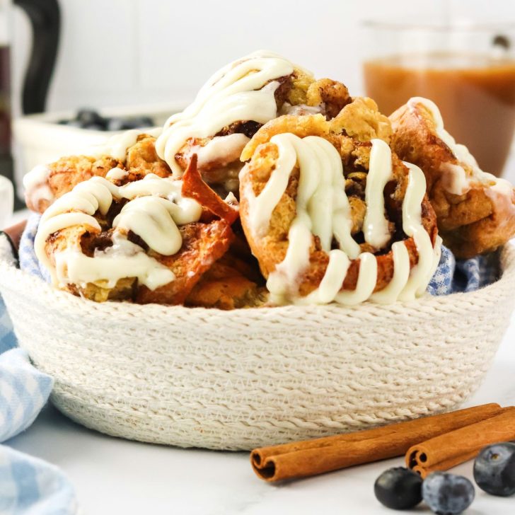 Sideview of a basket filled with beautifully baked cinnamon roll popovers topped with a cream cheese glaze - Hostess At Heart