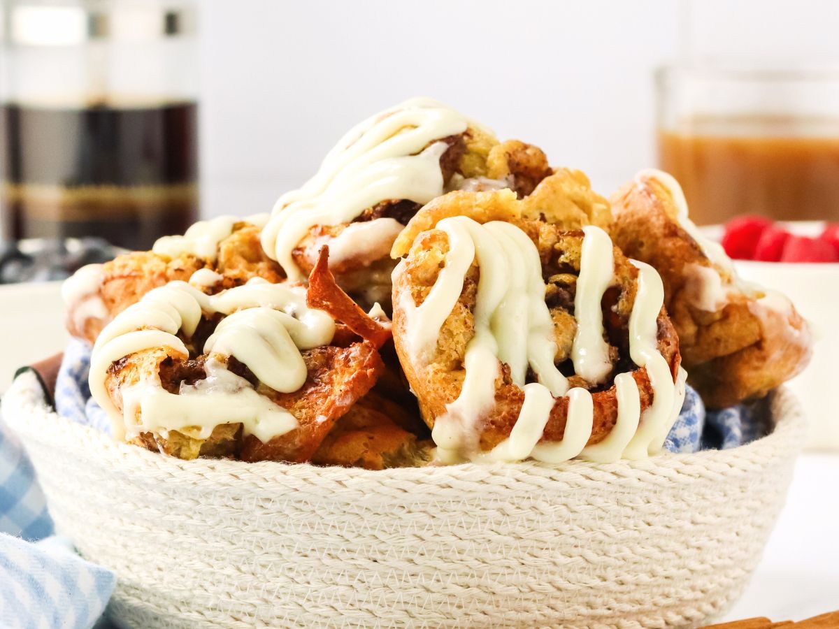 Sideview of a basket filled with baked cinnamon sugar popovers topped with a cream cheese glaze - Hostess At Heart