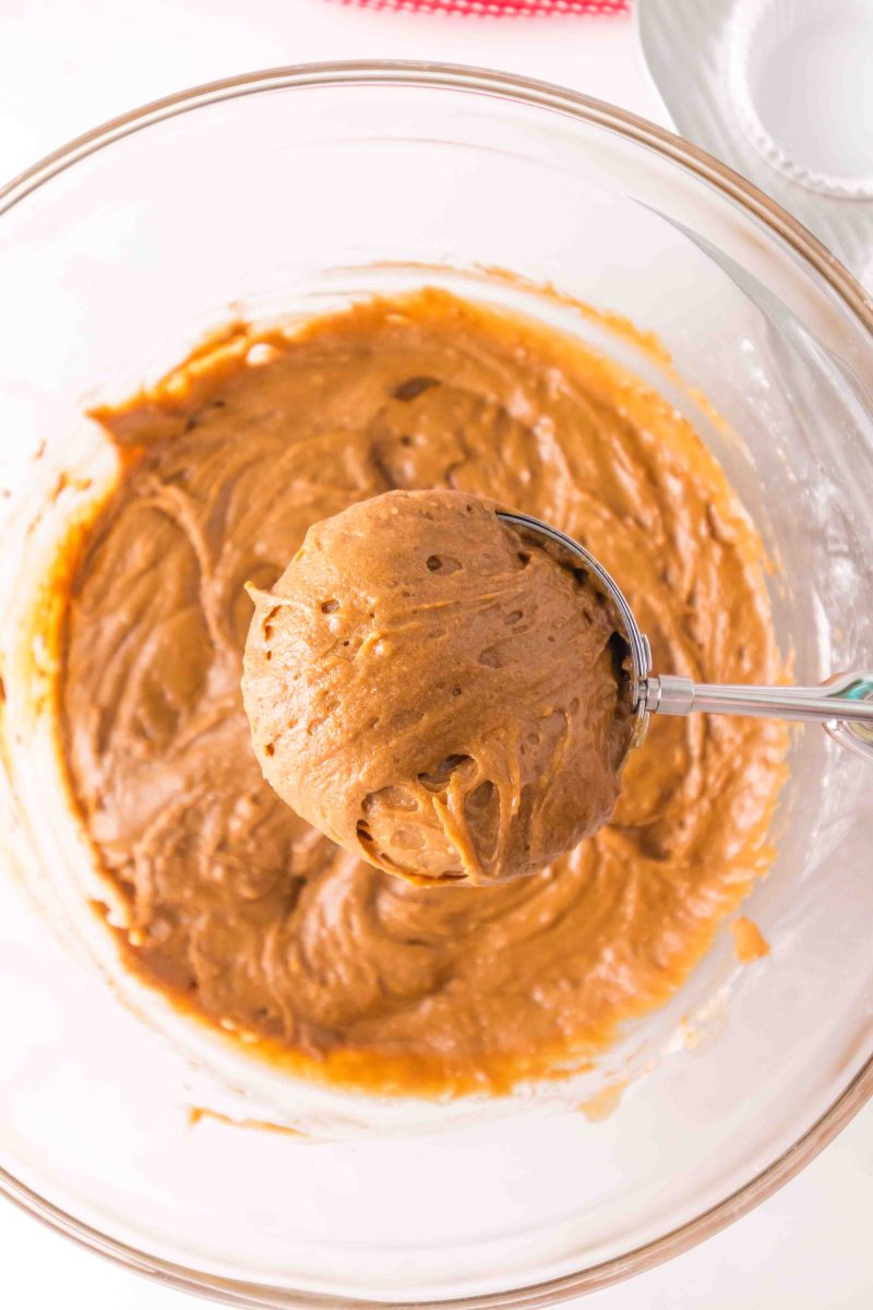 A scoop of muffin batter hovering over a bowl of muffin batter.