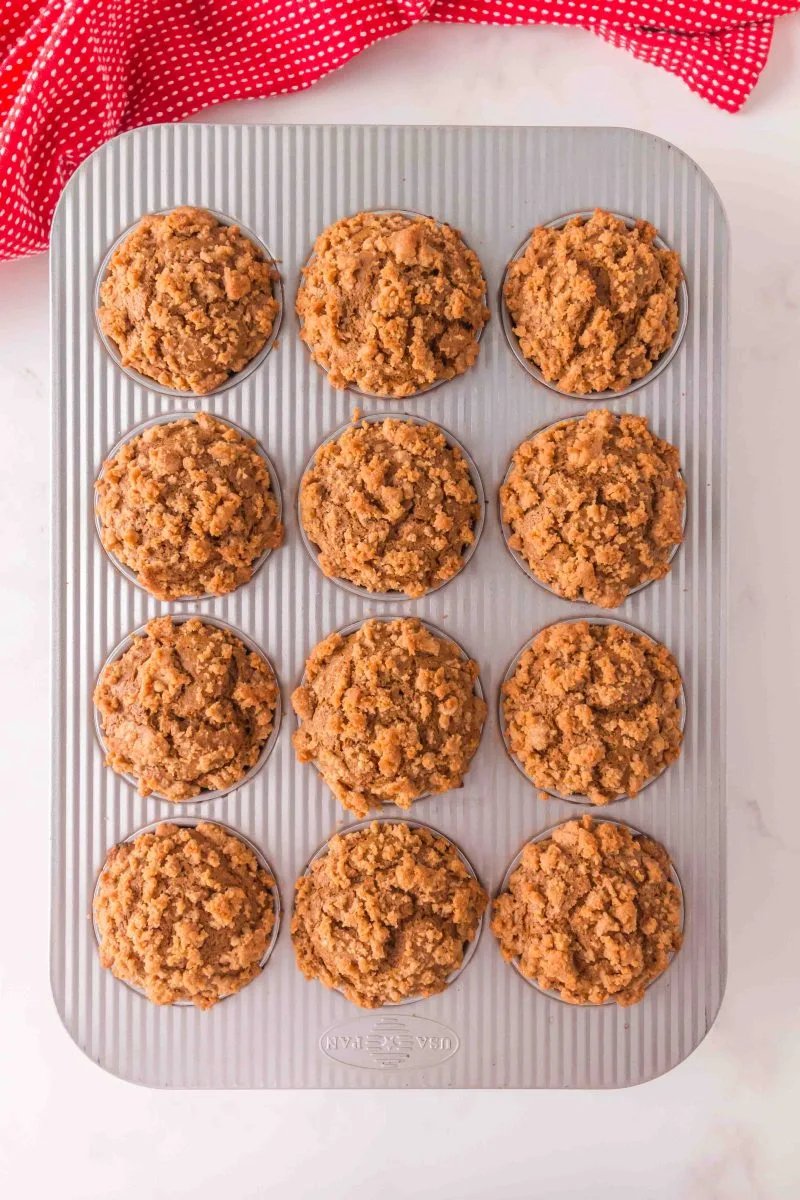 A muffin tin filled with muffin batter that's been topped with streusel. Hostess At Heart