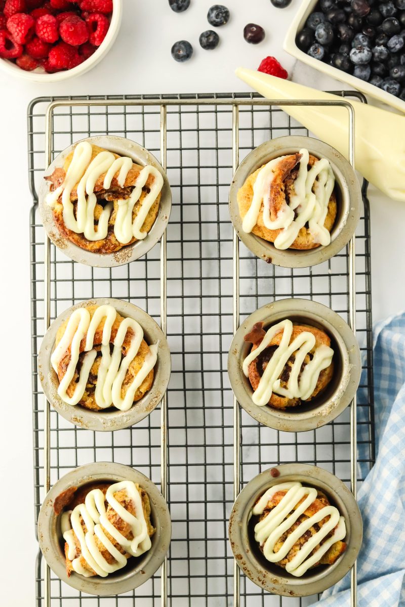 Top down view of a cooling rack topped with a popover pan filled with baked cinnamon popovers glazed - Hostess At Heart