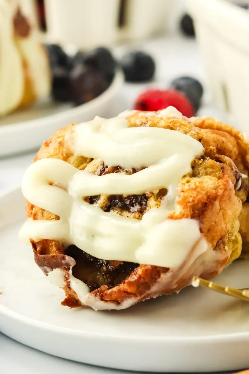 Sideview of a cinnamon filled popover topped with glaze sitting on a plate - Hostess At Heart