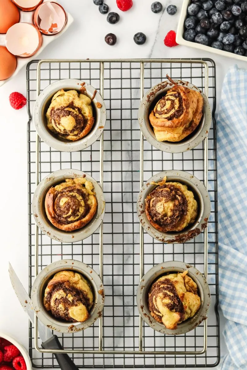 Cinnamon swirled popovers still in the pan sitting on a cooling rack - Hostess At Heart