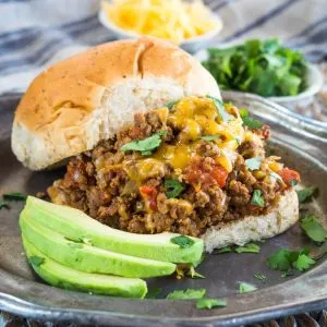 A table view of a bun topped with a large amount of spicy beef filling covered with melted cheese, and chopped cilantro - Hostess At Heart