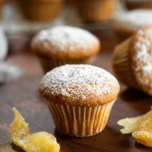 Tableview of a mini muffin dusted with powdered sugar and surrounded by crystallized ginger and more muffins.