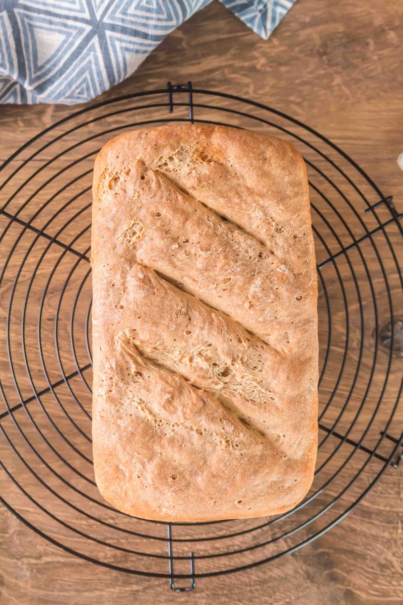 A loaf of rye bread cooling on a cooling rack. Top down image showing cracks in the loaf.