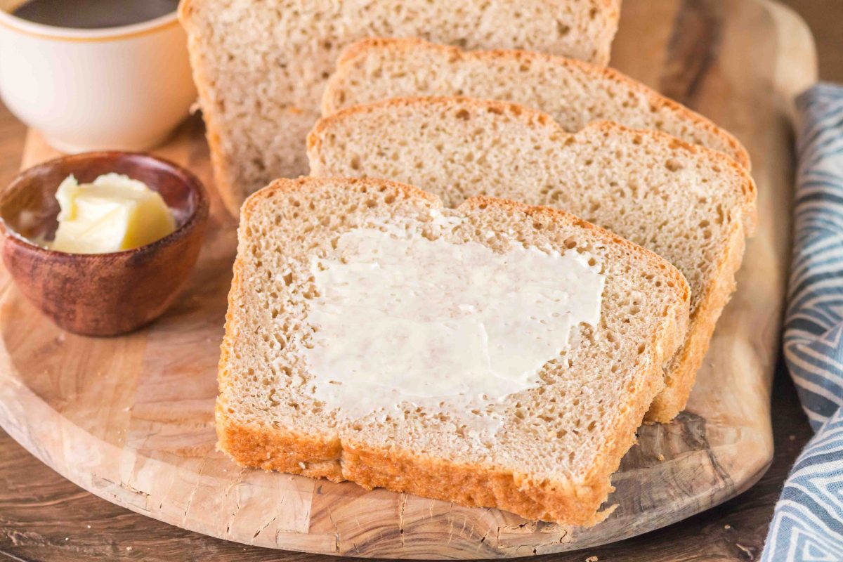 Close up of a buttered slice of homemade rye bread on a wooden cutting board.