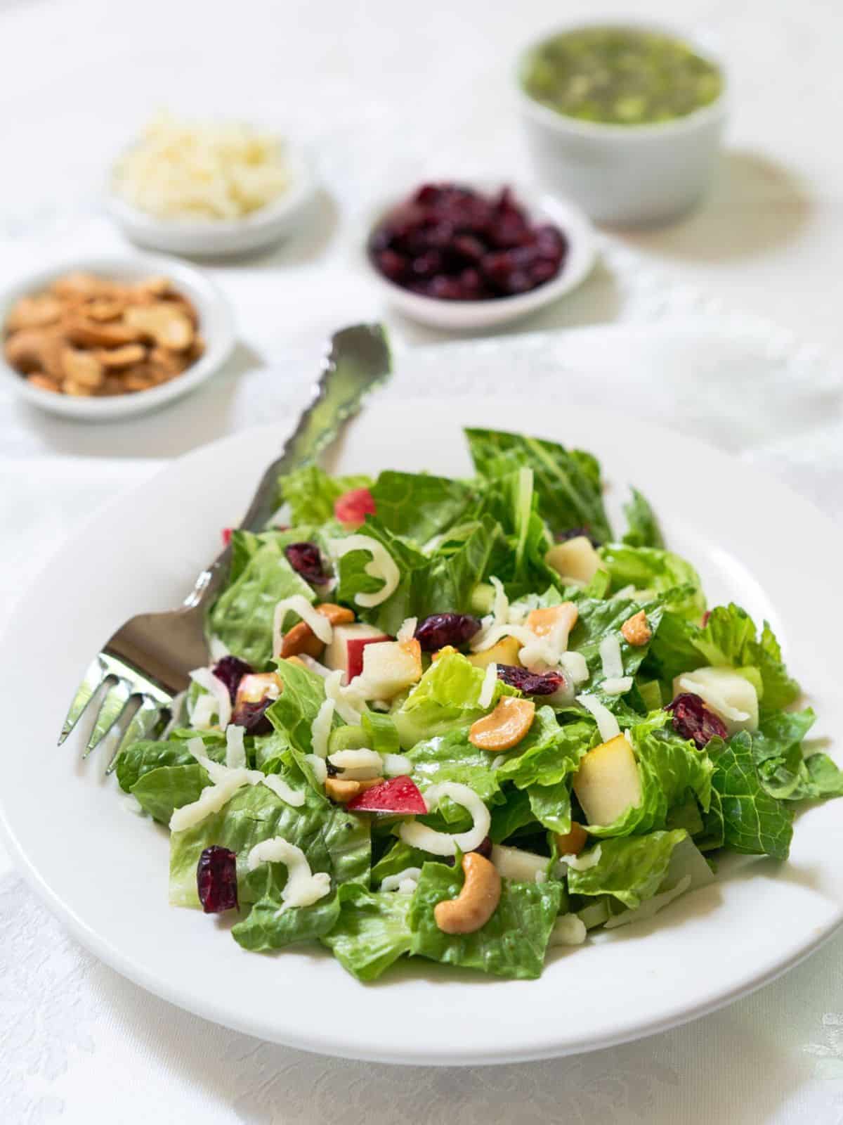 Front view of a vibrant green salad topped with crisp red apples, bartlett pears, craisins, and cashews - Hostess At Heart