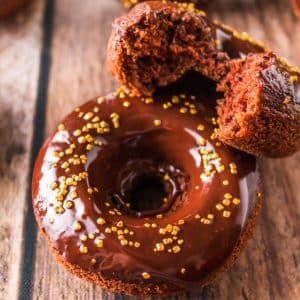 Top down view of a dark chocolate donut with chocolate ganache and sprinkles under a half of a donut showing a soft tender crumb - Hostess At Heart