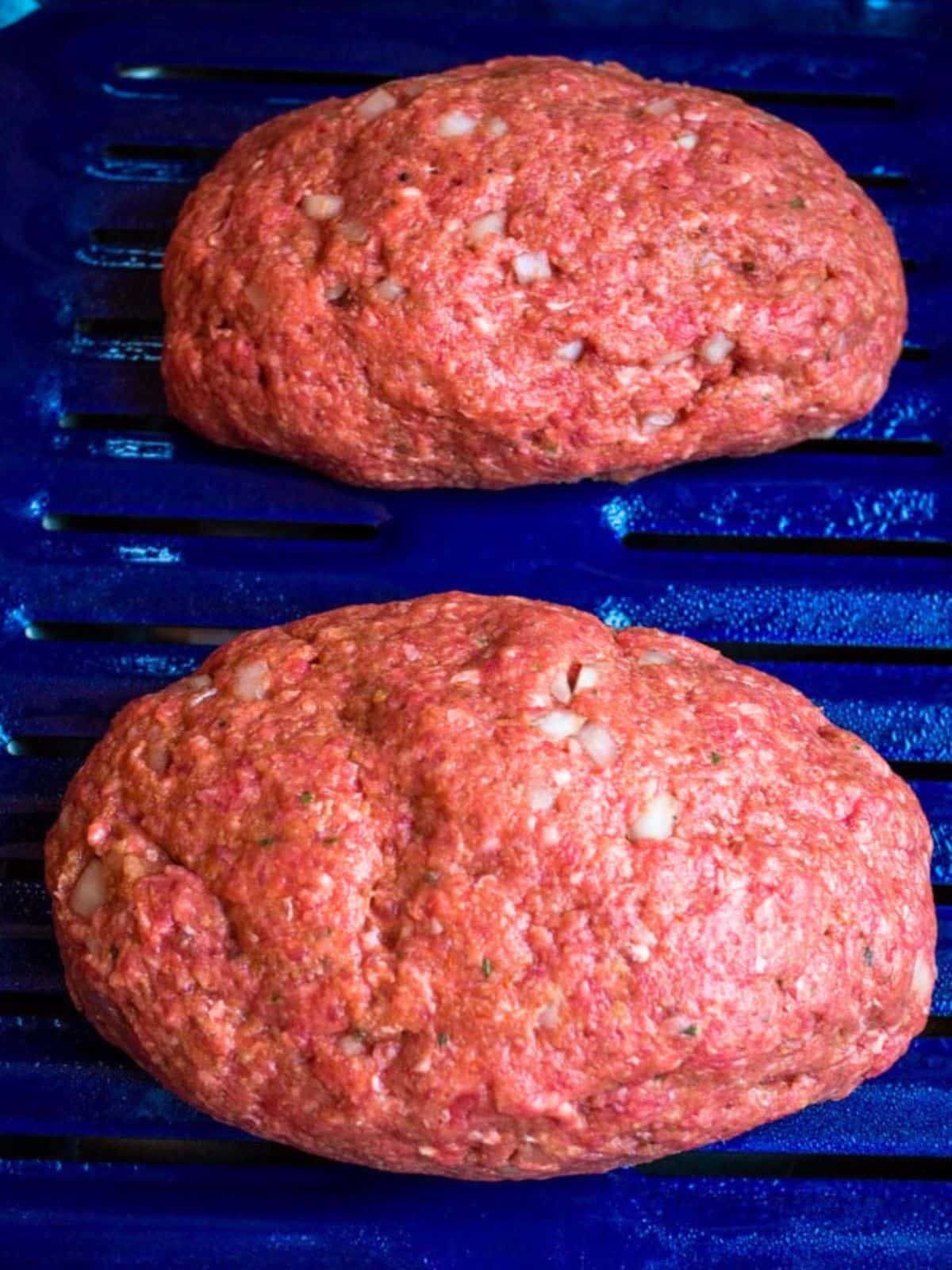 Top down view of two unbaked meatloaves sitting on a broiling pan. Hostess At Heart