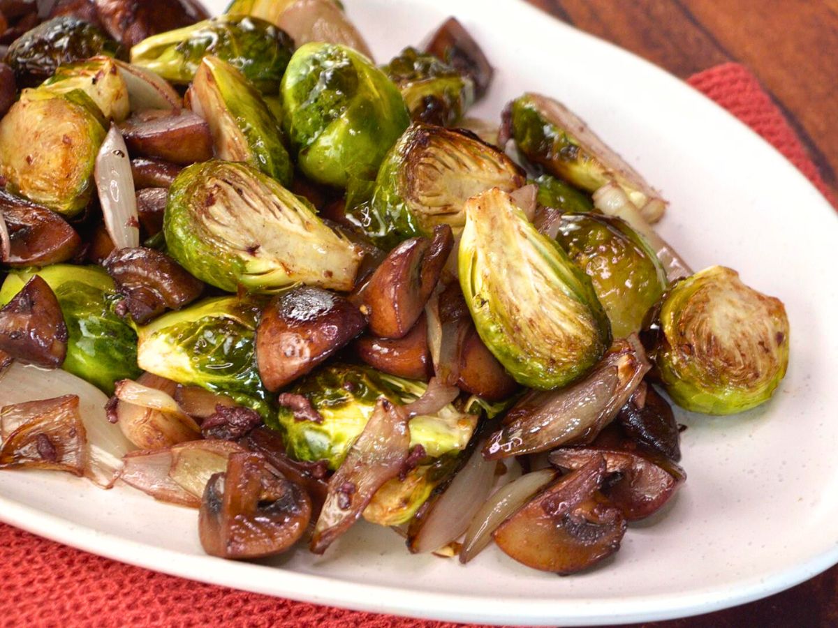 Sideview of a platter holding roasted brussel sprouts, shallots and mushrooms in a wine sauce.