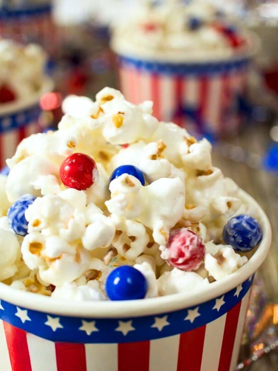 Tableview closeup of almond bark candy coated popcorn decorated with red and blue candy pieces for the 4th of July - Hostess At Heart