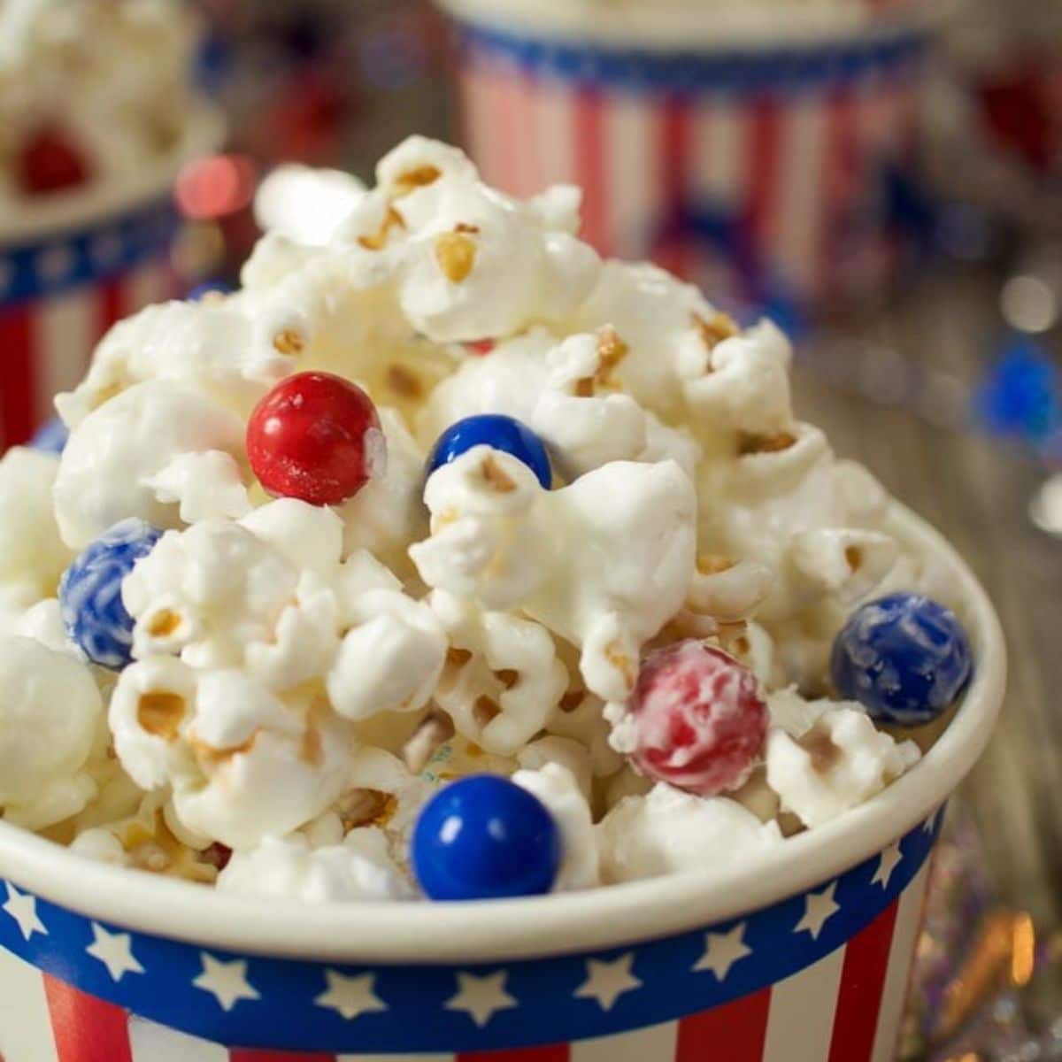 A close up tableview image of a cup of candy-coated popcorn decorated with red and blue candy pieces - Hostess At Heart