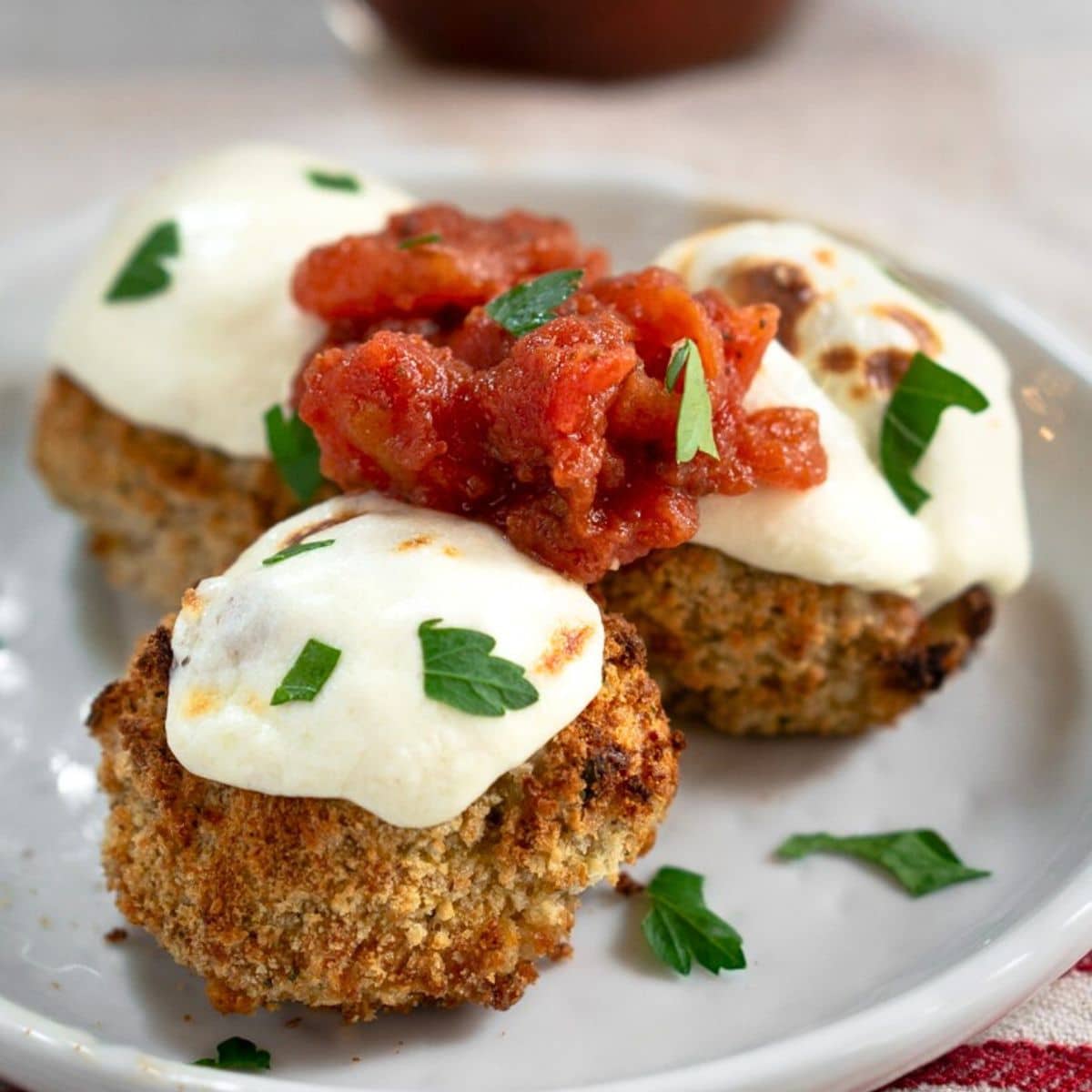 Angled view of a baked meatball topped with toasted mozzarella and fresh tomato marinara - Hostess At Heart