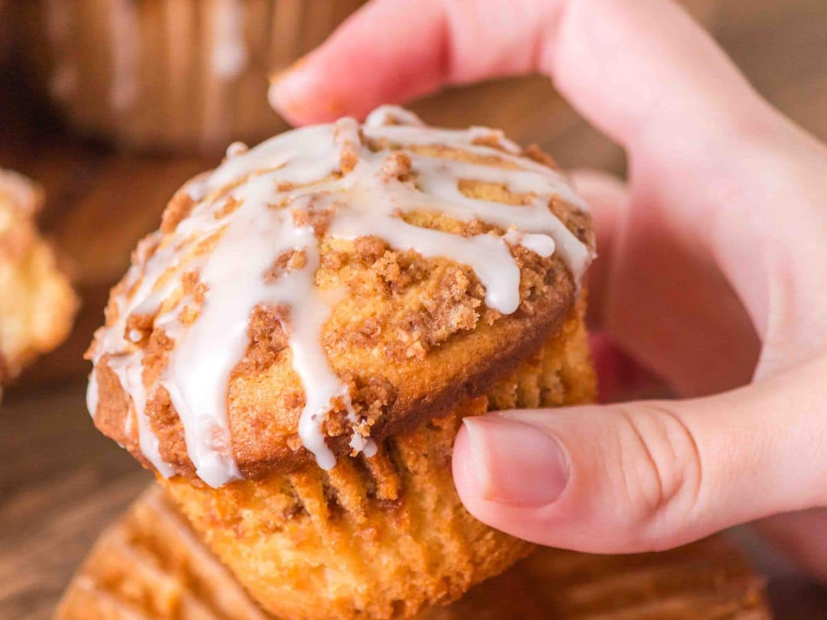 A hand holding a glazed muffin topped with a cinnamon streusel - Hostess At Heart