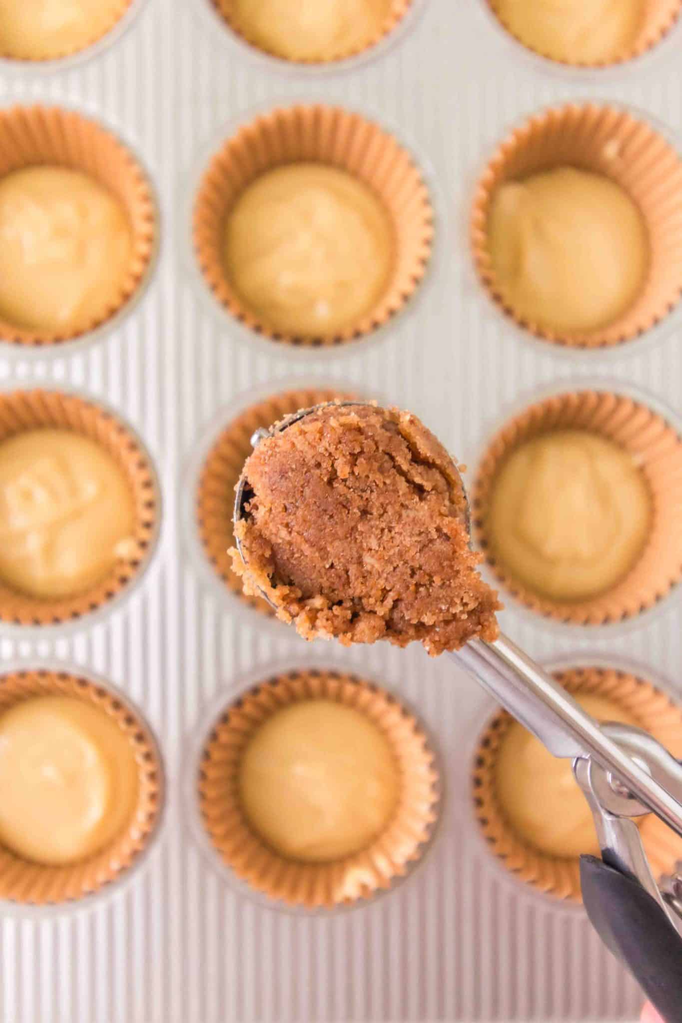 A scoop filled with cinnamon streusel hovering over a muffin tin - Hostess At Heart