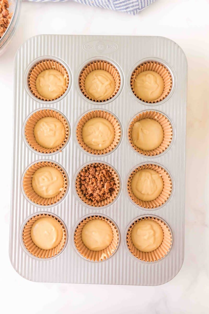 Top down view of a muffin tin filled with cinnamon roll batter. The middle one is topped with streusel.