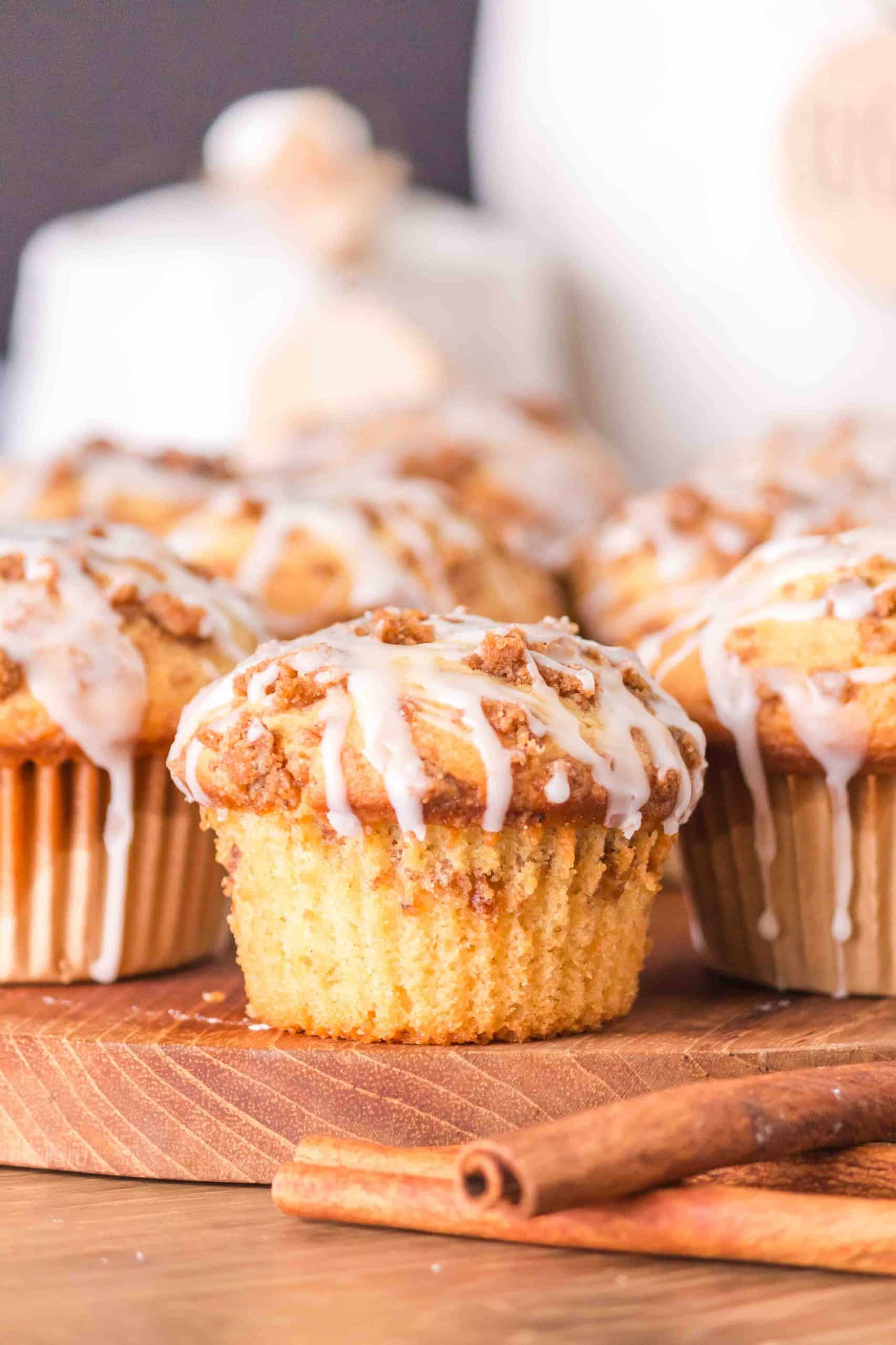 Sideview of cinnamon streusel muffins on a cutting board with glaze dripping down the side. Hostess At Heart