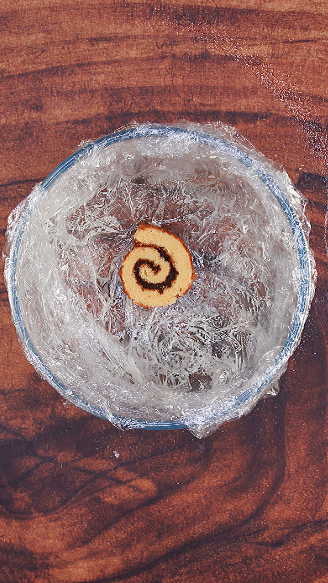 A plastic wrap-lined bowl with one swiss roll slice swirled with chocolate buttercream set in the bottom. Hostess At Heart