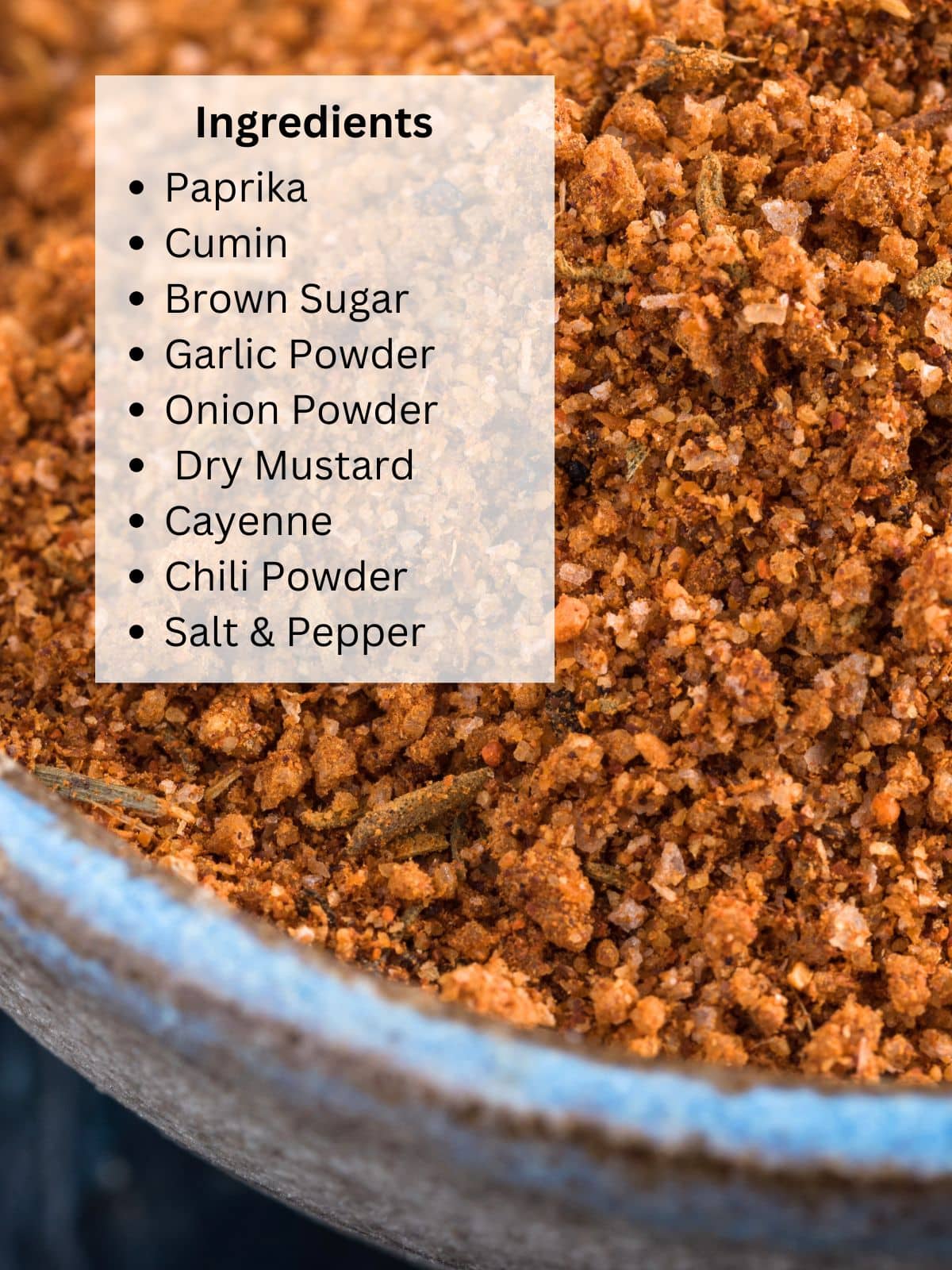 A bowl filled with homemade spice blend for bbq and roasting. A list covers part of the image listing the ingredients including brown sugar, paprika, cayenne, chili powder, onion powder, garlic powder, dry mustard, cumin, salt, and pepper. Hostess At Heart